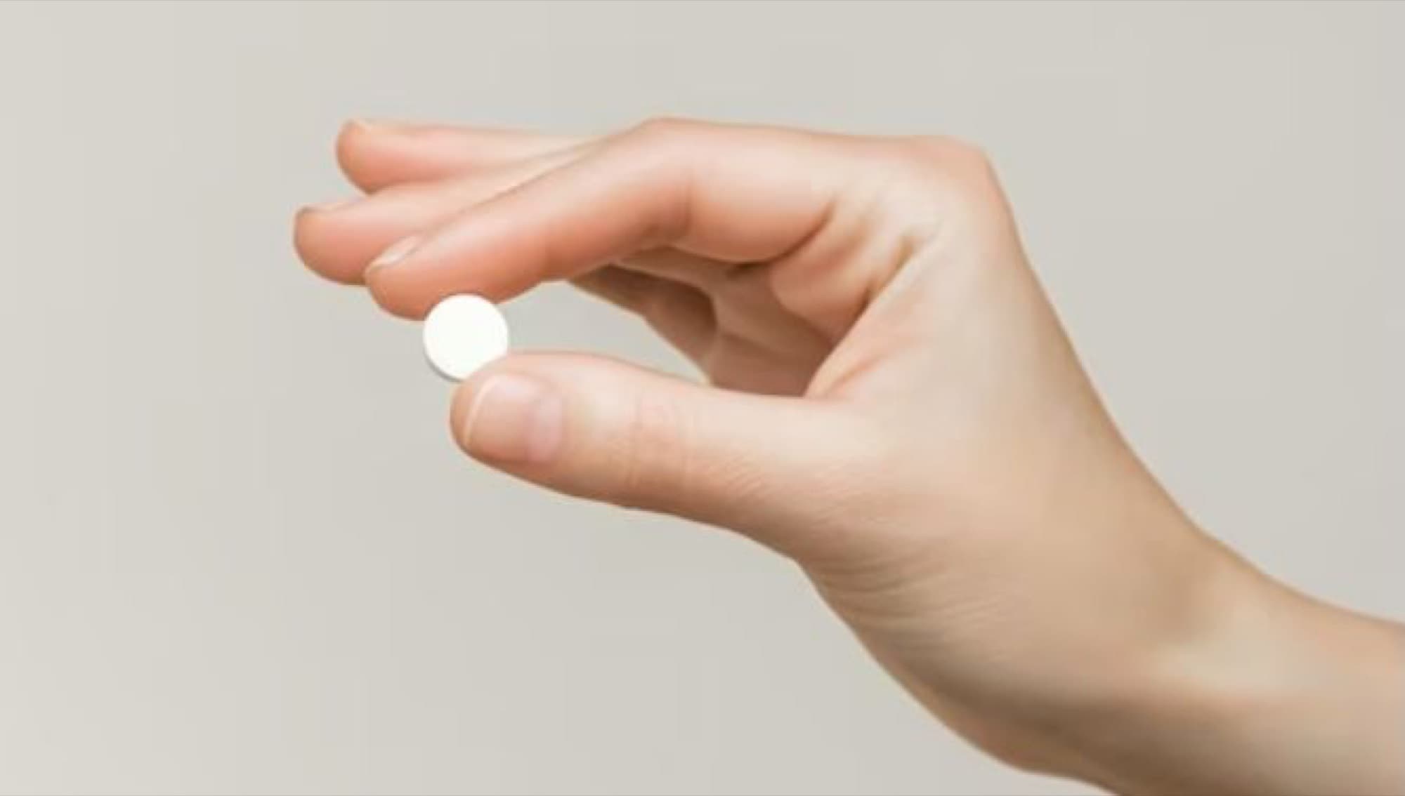 A hand holding a single white tablet against a pale background