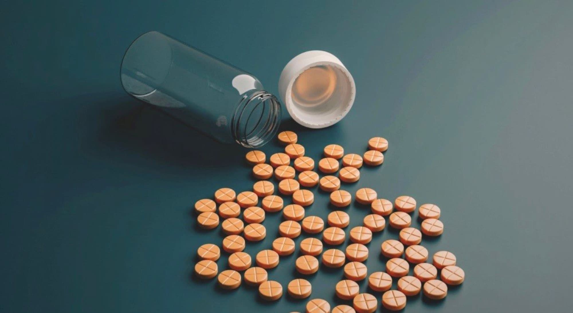 An open pill bottle with orange tablets spilled across a dark table