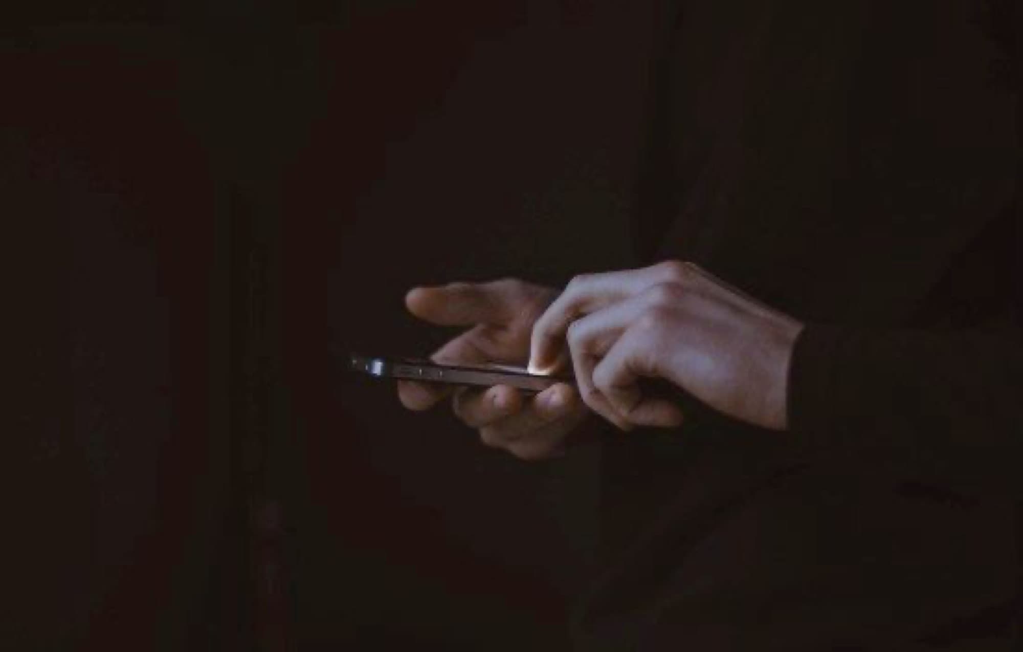 Hands holding a lit phone in a dark room